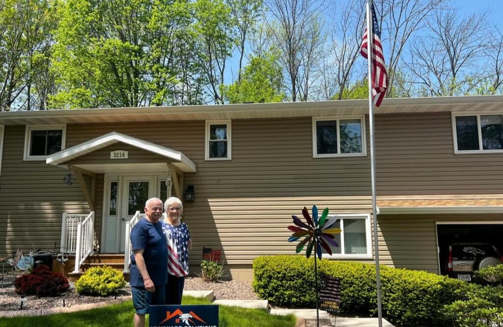 Happy Couple on front of their new Roof Replaced home with Vanguard Roofing & Siding yard sign