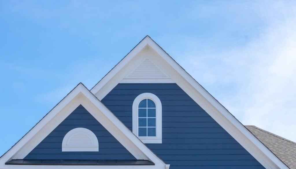 White attic window vent on blue siding, gable, corbel, louver on a new construction luxury American single family home in the East Coast USA with blue sky background