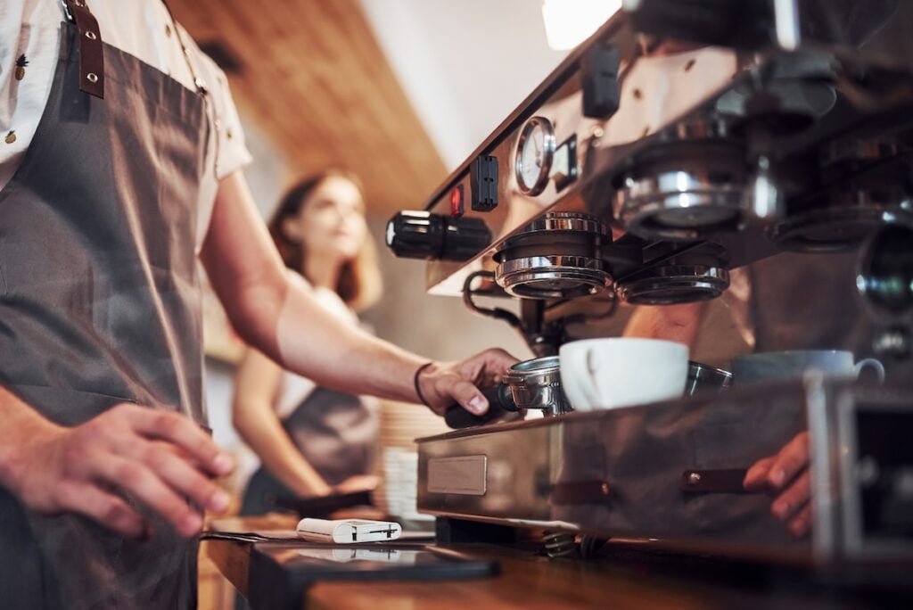 Process of making fresh drink. With machine. Two young cafe workers indoors