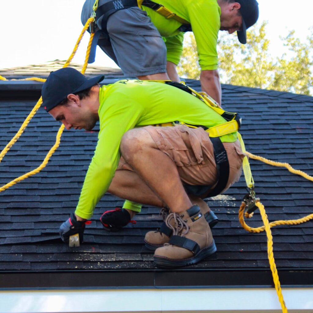 Roofing professionals installing shingles with safety harnesses for a roofing company near me