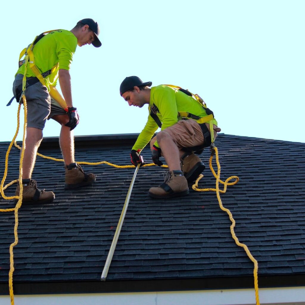Roofing professionals inspecting a shingle roof with safety harnesses for a roofing company near me