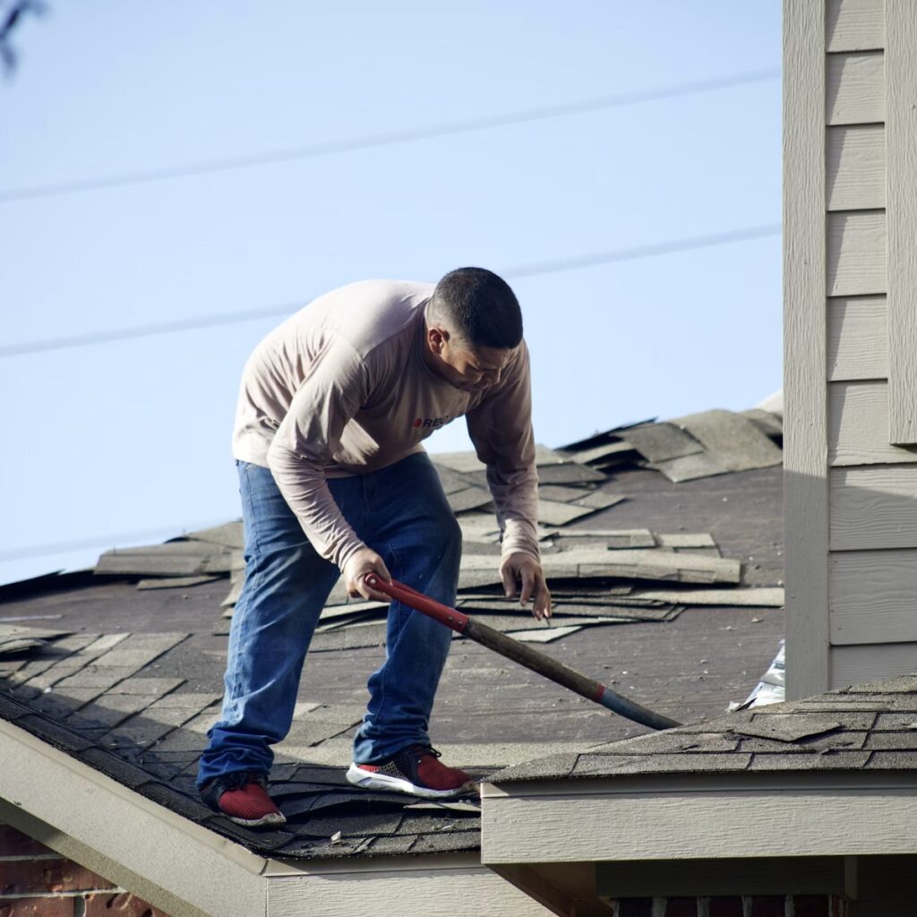 Roofing professional removing damaged shingles from a residential roof for a roofing company near me