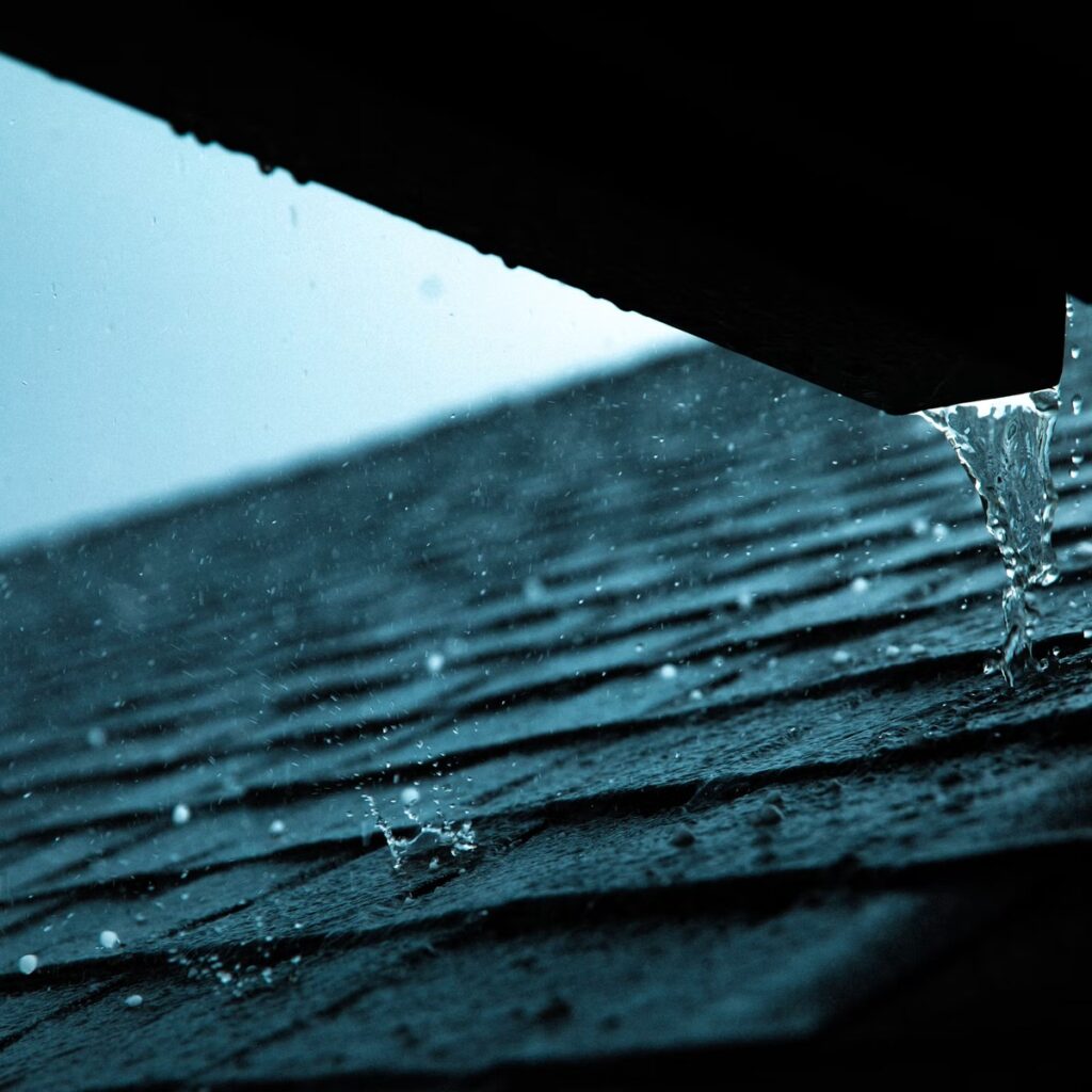 Rainwater running off a wet shingle roof for a roofing company near me